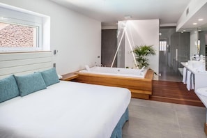 A modern bedroom with a large bed, a wooden platform bathtub, a small bedside table, and a large window with a view of rocks. - Hyde Park Lane Villas (Tías)