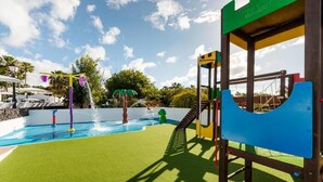 A playground with a slide and climbing structures, a pool with water features, and a green artificial turf surface. - Hyde Park Lane Villas (Tías)