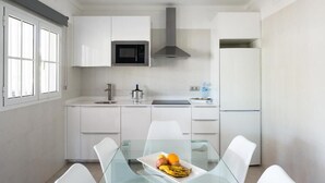 A modern kitchen with white cabinets, a microwave, a stainless steel range hood, and a refrigerator. There is a glass dining table with chairs and a fruit plate on it. - Hyde Park Lane Villas (Tías)