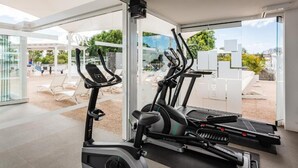 A modern gym with cardio equipment, large windows, and a view of the outdoor area. - Hyde Park Lane Villas (Tías)
