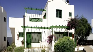 Un bâtiment blanc agrémenté de touches de vert, un espace extérieur couvert et un petit jardin.