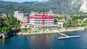 A hotel with a central red structure, surrounded by a waterfront and greenery, with mountains in the background. - Splendid (Baveno)