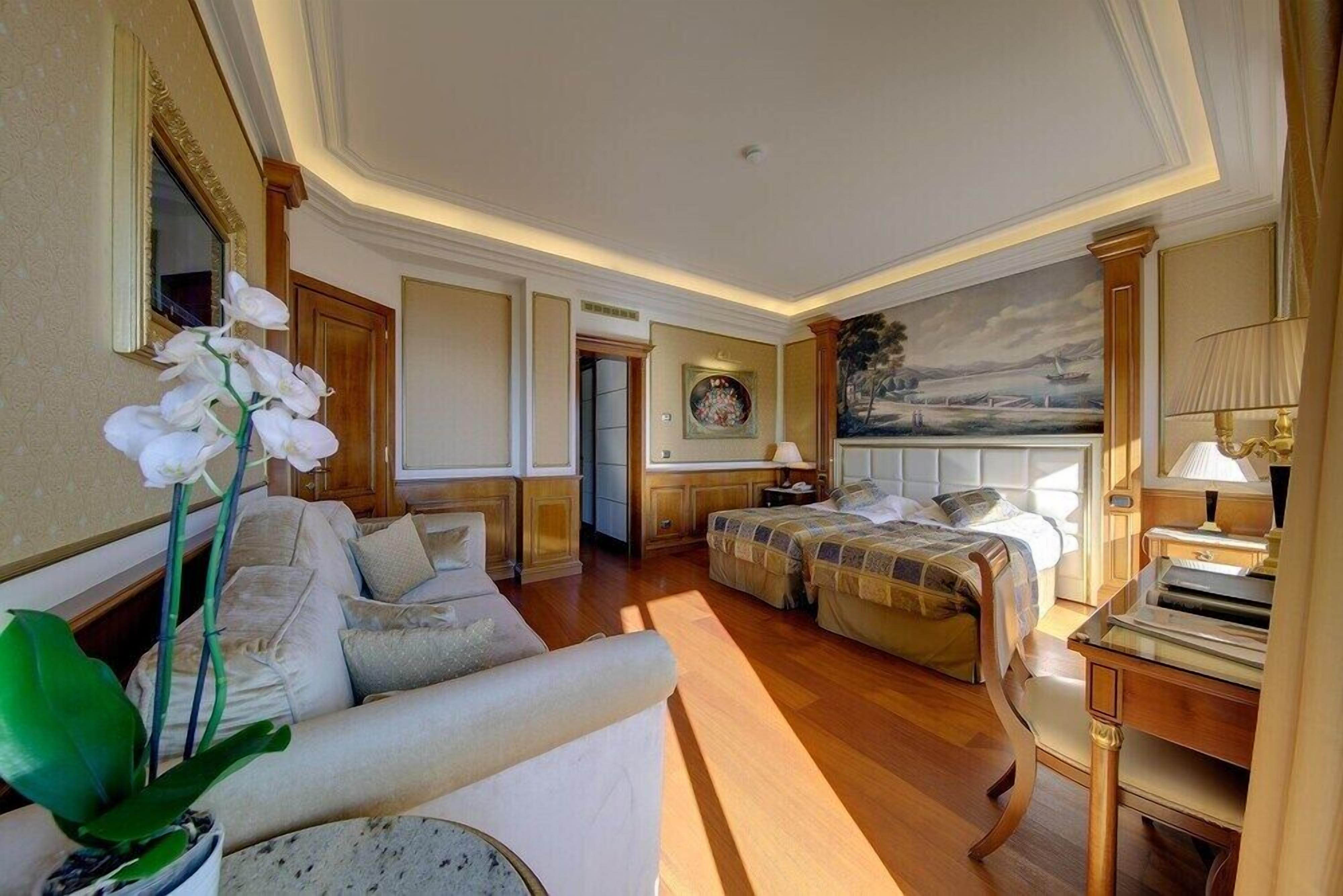 A hotel room with a sofa, a bed, a desk, and a painting on the wall.