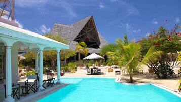A swimming pool with lounge chairs and umbrellas, a covered seating area, and a distinctive pyramid-shaped building in the background.