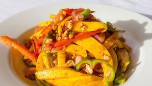 Un plat composé de tranches de mangue, de poivrons rouges et de noix, présenté sur une assiette blanche.