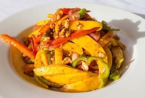 A dish with sliced mango, red bell peppers, and nuts on a white plate.