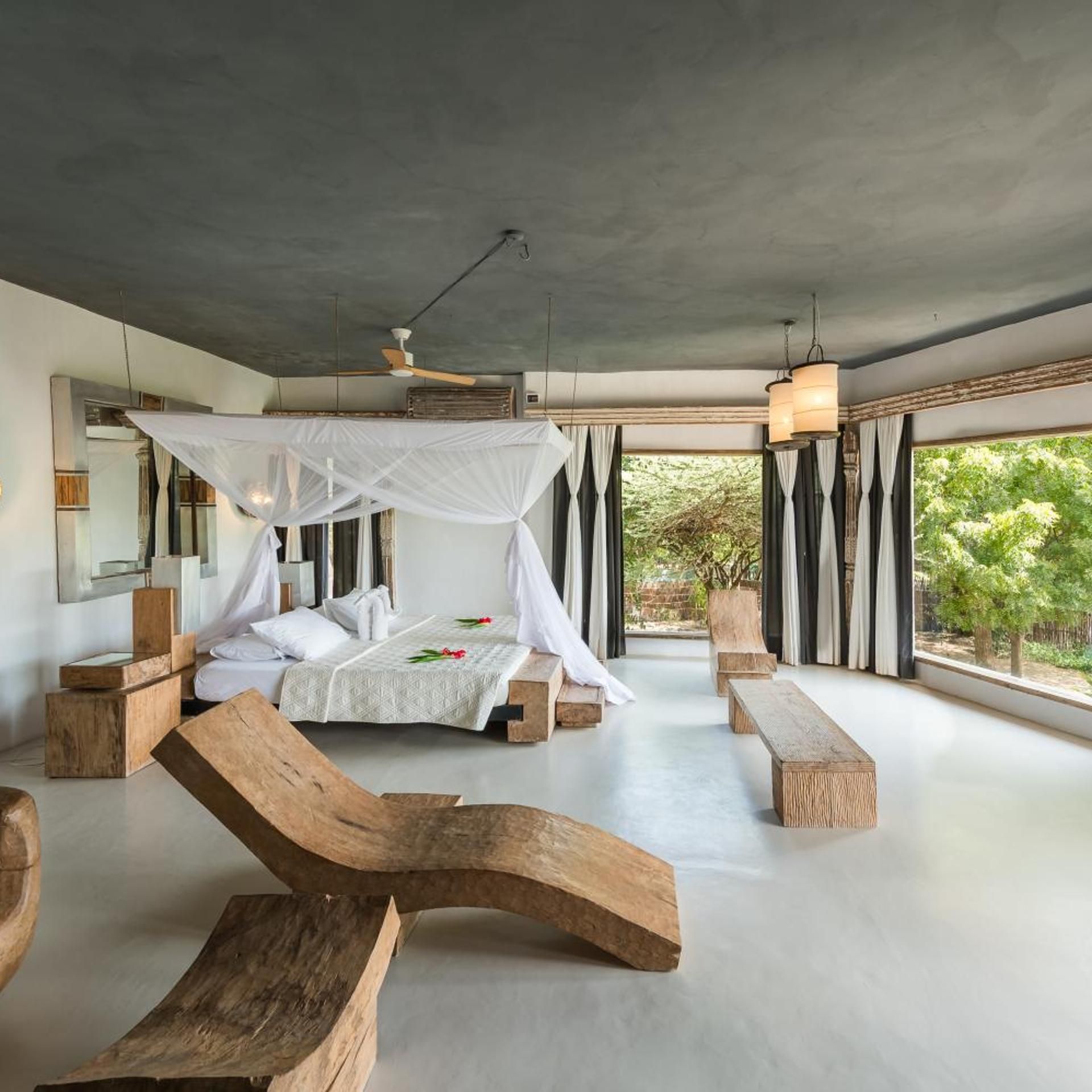 Une chambre moderne avec un grand lit, un ventilateur de plafond et une vue sur la verdure environnante.