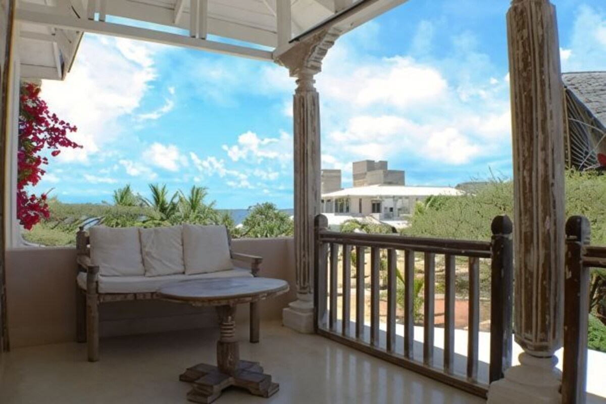 A covered outdoor seating area with a view of the ocean and buildings.