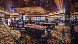 Ein Casino mit mehreren Blackjack-Tischen, einer farbenfrohen Deckenmalerei und einem gemusterten Teppich.