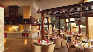 Ein Restaurant mit Korbstühlen, einer zentralen Bar und Blick ins Freie.