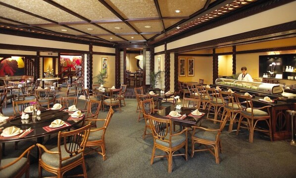 A restaurant with multiple dining tables and chairs, a central serving area, and a traditional architectural design. - Sun City Hotel (Moses Kotane)