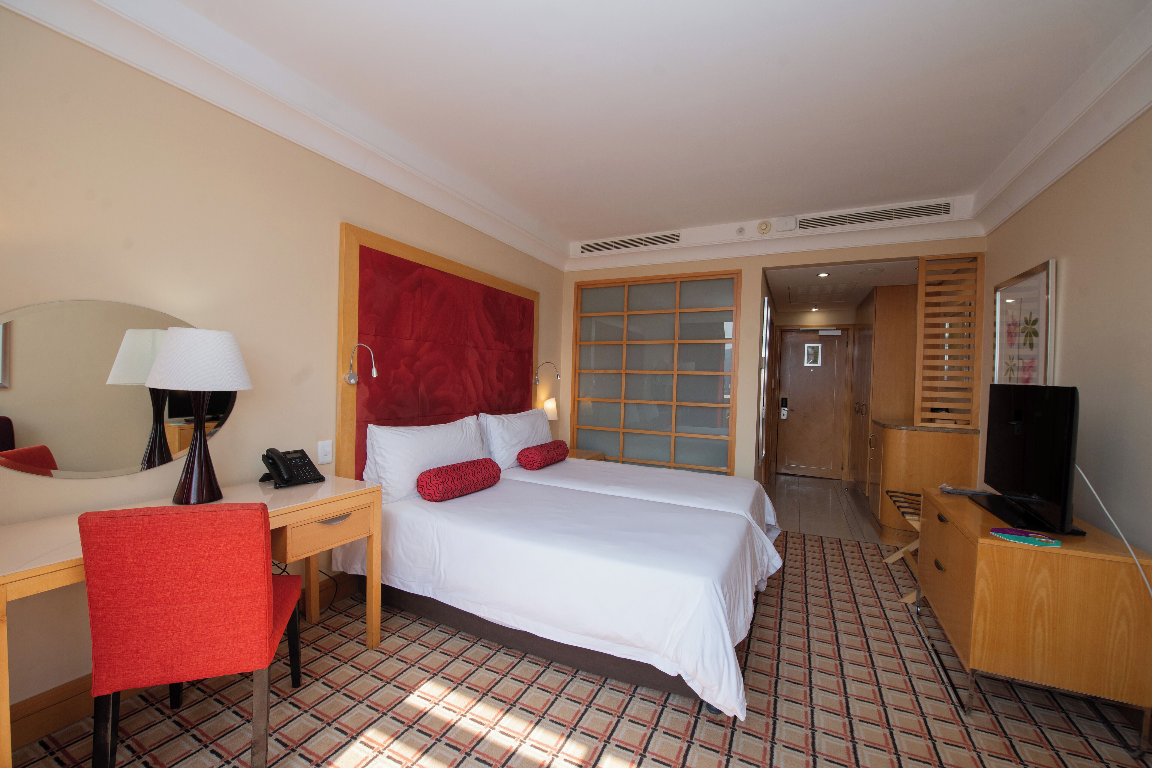 A hotel room with a bed, desk, chair, TV, and a door leading to another room.