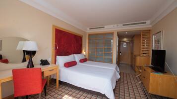 A hotel room with a bed, desk, chair, TV, and a door leading to another room.