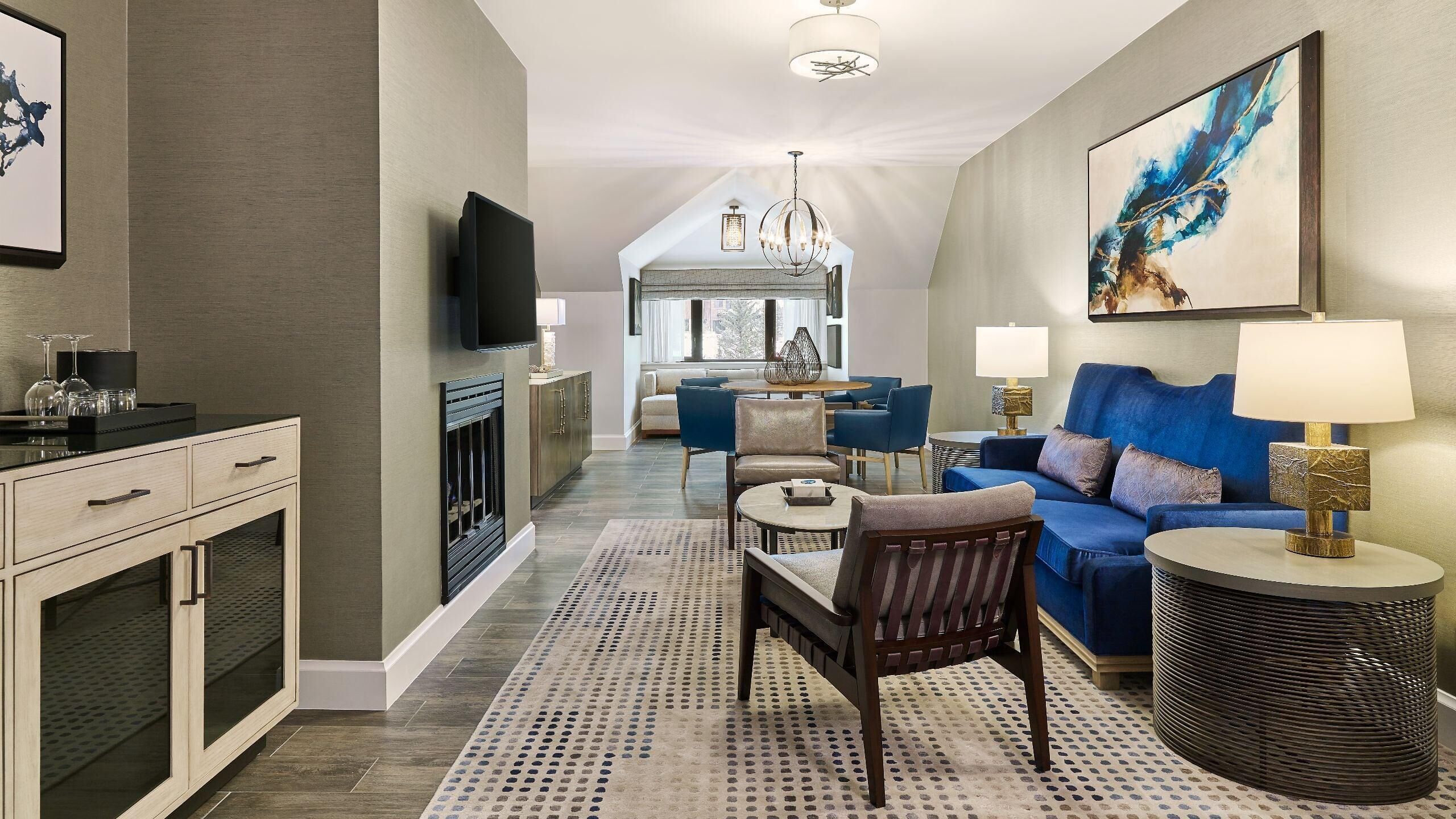 Une chambre d’hôtel moderne avec un coin repas, une cheminée, un canapé bleu et un grand tableau.