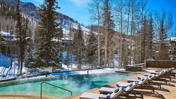 A hot tub surrounded by lounge chairs, with a snowy mountain backdrop.