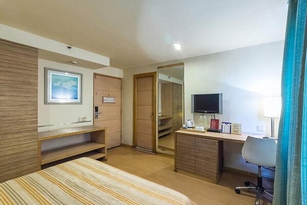 A hotel room with a bed, a desk, a television, a mirror, and a wardrobe. - Mapple Express Bangalore (Bengaluru)