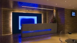 A reception area with a modern design, featuring a reception desk, a flat-screen TV, and a seating area with a glass table and chairs. - Mapple Express Bangalore (Bengaluru)