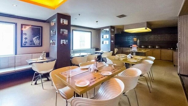A modern dining area with multiple tables and chairs, a kitchen area with a stove and counter, and large windows allowing natural light. - Mapple Express Bangalore (Bengaluru)