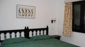 Une pièce avec un lit, un tableau accroché au mur, une fenêtre avec des rideaux et une table de chevet.
