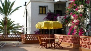 Une terrasse extérieure avec un parasol jaune, des chaises en bois et un banc.