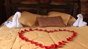 A bed with a heart-shaped decoration made of red rose petals and two swan-shaped pillows. - Sumak Pakari Hosteria (Gualea)