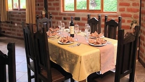 A dining area with a table set for two, featuring a yellow tablecloth, wooden chairs, and a bottle of wine. - Sumak Pakari Hosteria (Gualea)