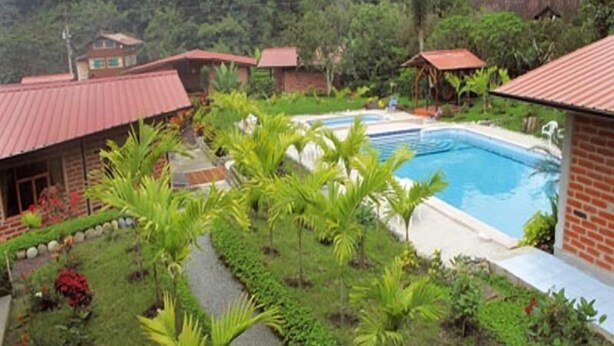 A pool surrounded by lush greenery and red-roofed buildings. - Sumak Pakari Hosteria (Gualea)