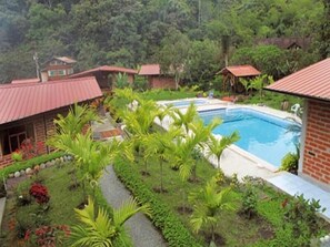 A pool surrounded by lush greenery and red-roofed buildings.
