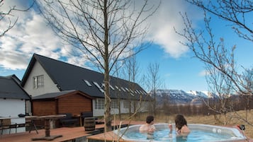 A hot tub in a backyard with a house and mountains in the background.