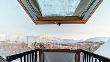 Une vue à travers un puits de lumière doté d’un cadre en bois, donnant sur un paysage enneigé avec des montagnes et un ciel dégagé.