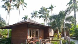 A wooden cabin with a porch, surrounded by lush greenery and palm trees. - Gajapuri Resort Spa (Ko Chang)