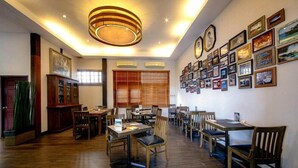 A spacious dining area with wooden tables and chairs, a large chandelier, and a wall decorated with framed pictures. - Gajapuri Resort Spa (Ko Chang)
