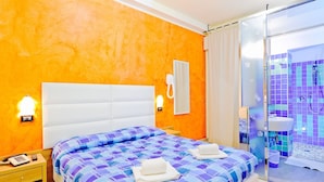 Une chambre d’hôtel avec un grand lit, un téléphone sur la table de chevet, une table de chevet et une salle de bain dotée d’une douche à parois de verre.
