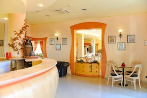 A hotel lobby with a reception desk, a dining area with chairs, and framed pictures on the walls. - Vannucci Hotel (Rimini)