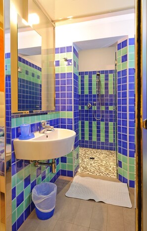 Casa de banho com lavatório, espelho e área de duche, com azulejos azuis e verdes.
