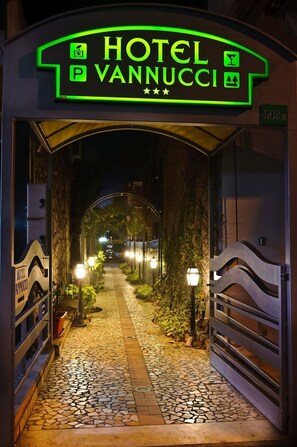 Entrada de hotel con un letrero de neón, un camino pavimentado y farolas.