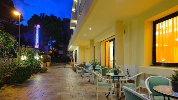 Une terrasse d’hôtel avec des sièges en plein air, une enseigne au néon et un intérieur bien éclairé.