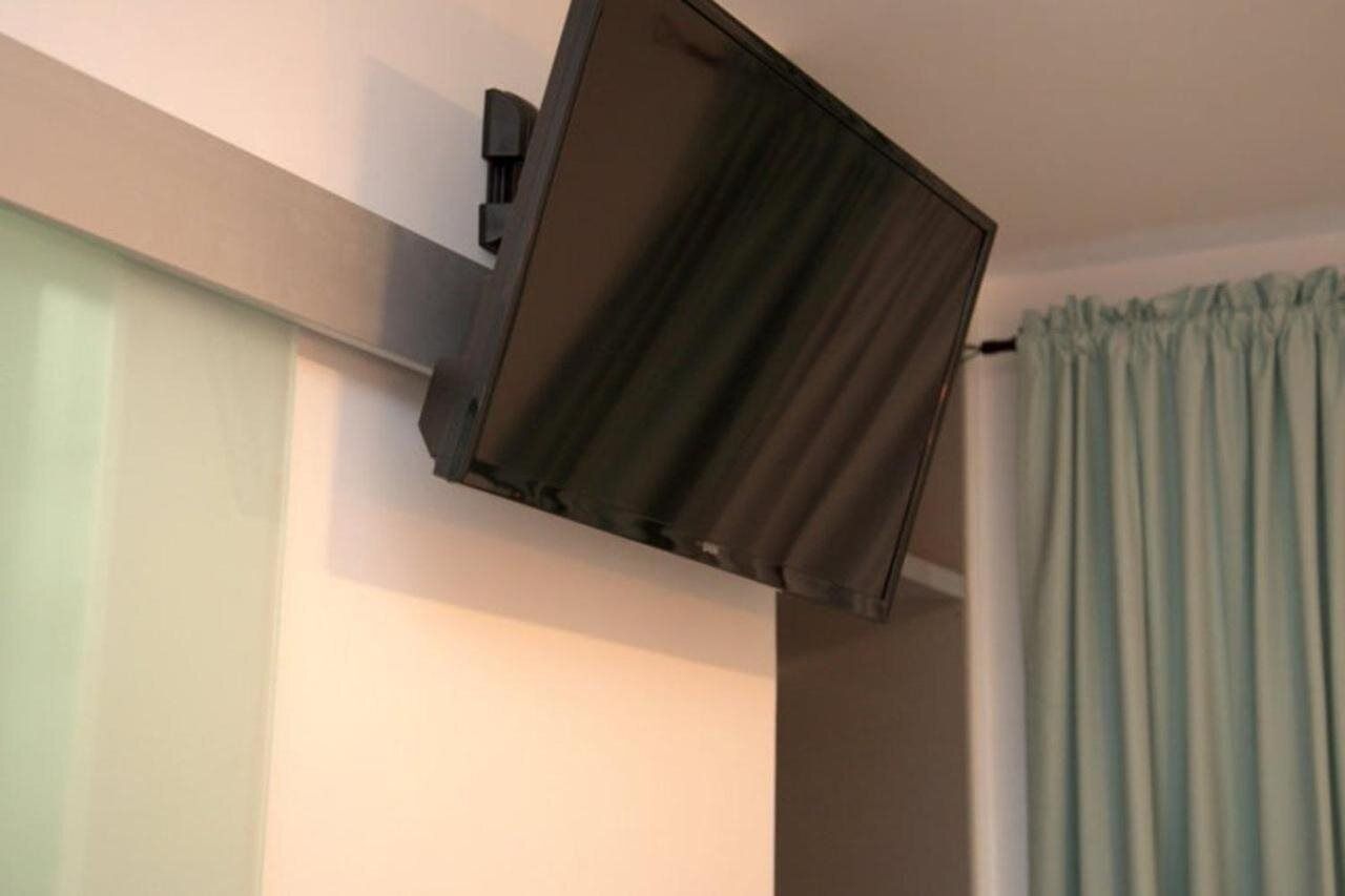 A room with a ceiling-mounted television and a light blue curtain.