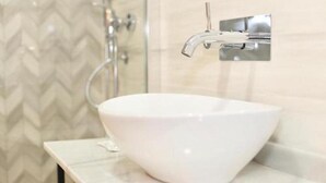 Un baño con un lavamanos blanco tipo tazón, grifo cromado y ducha.