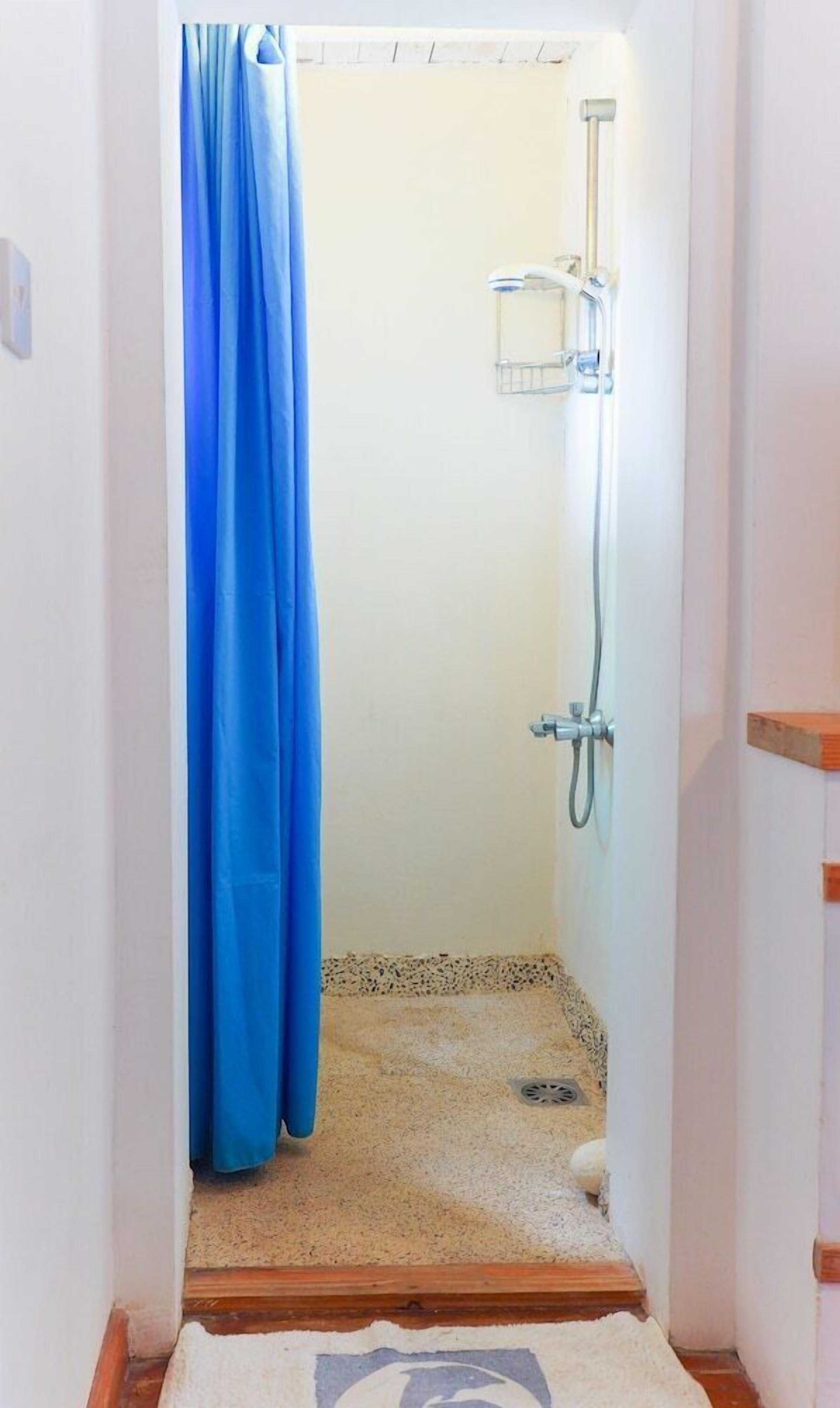 A narrow bathroom with a shower, a blue curtain, and a small rug.