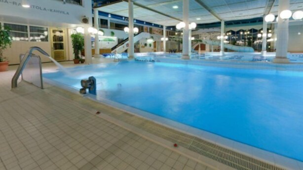 Une piscine intérieure à l’eau claire, entourée d’un sol carrelé et surmontée d’un plafond aux panneaux bleus.
