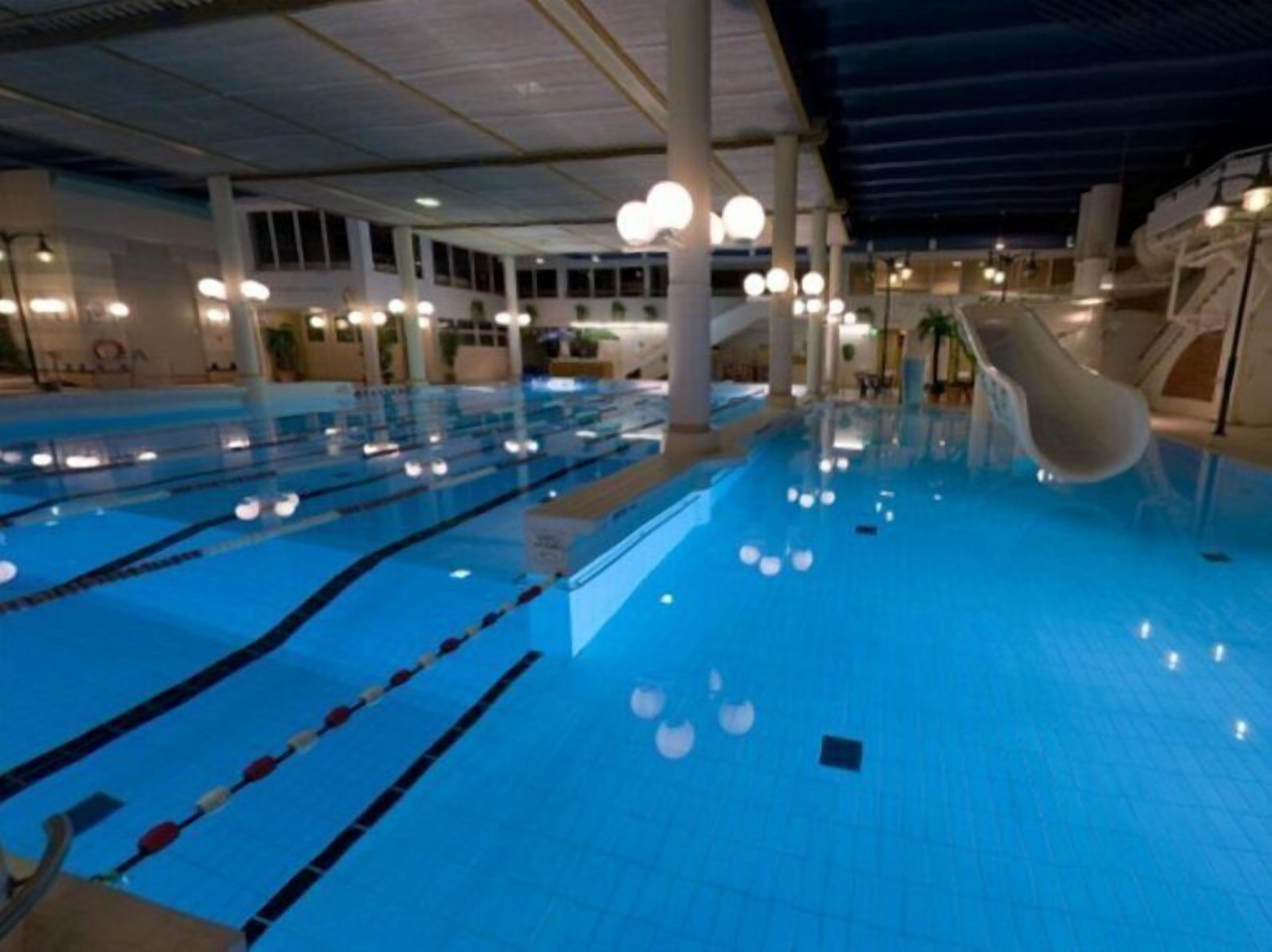 An indoor swimming pool with multiple lanes, a water slide, and a covered roof structure.