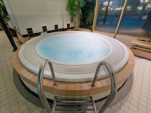 A hot tub with a circular design, surrounded by a tiled floor and a wooden border. - Sport Spa Hotel Vesileppis (Leppavirta)