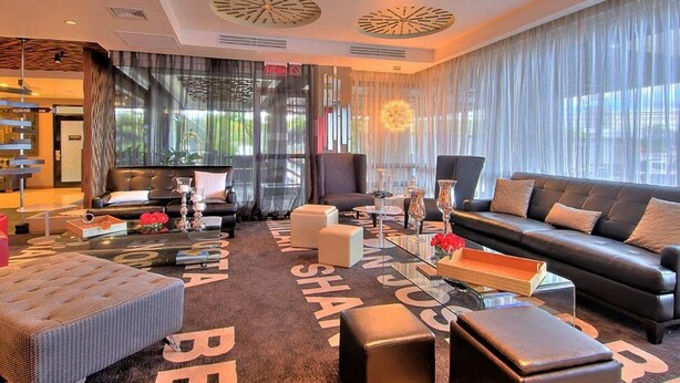 A modern living room with a black leather sofa, a glass coffee table, and a patterned rug. - Tryp San Jose Sabana (San José)