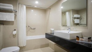 A modern bathroom with a bathtub, a sink, and a toilet. There are towels on a rack and a mirror above the sink. - Clayton Hotel Silver Springs (Cork)