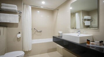 Un baño moderno con bañera, lavamanos e inodoro. Hay toallas en un perchero y un espejo sobre el lavamanos.