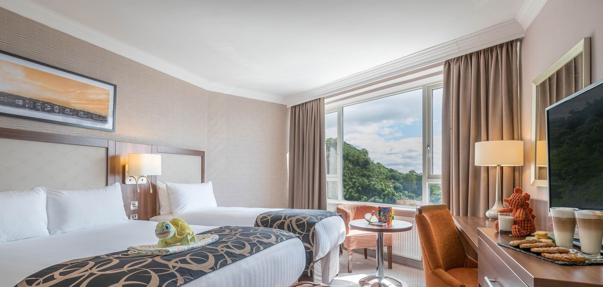 A hotel room with two beds, a dining area, a TV, and a view of the outdoors.