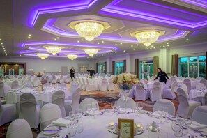 Een balzaal met ronde tafels, witte tafelkleden en kroonluchters.