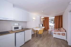A compact kitchen with a microwave, toaster, and small refrigerator. There is a dining area with a table and chairs, and a sofa with a patterned cover. - Sol Parc Apartments (Mercadal)