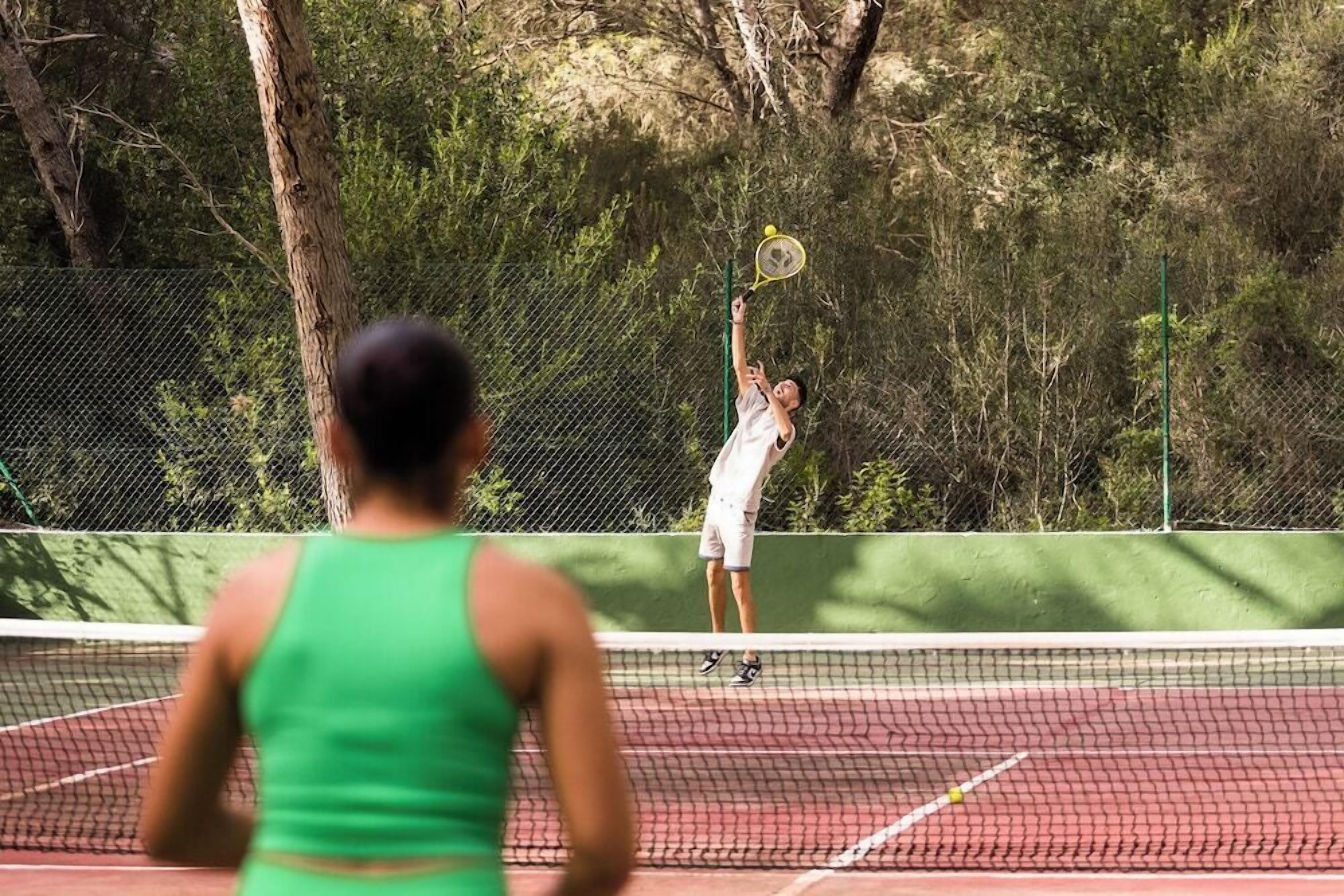 Una cancha de tenis con una red, rodeada de árboles y una valla.